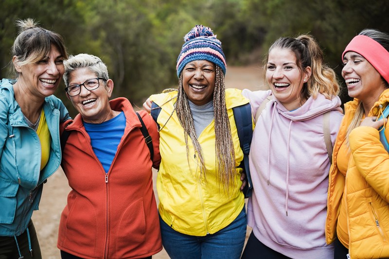 5 individuals of varying ages and races huddle together on a trail smiling